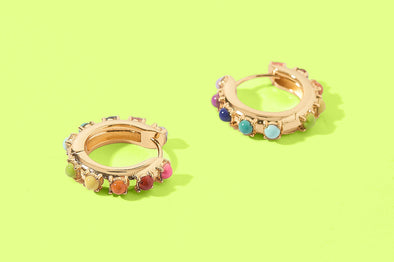 Pair of gold hoop earrings with colorful stones on a green background