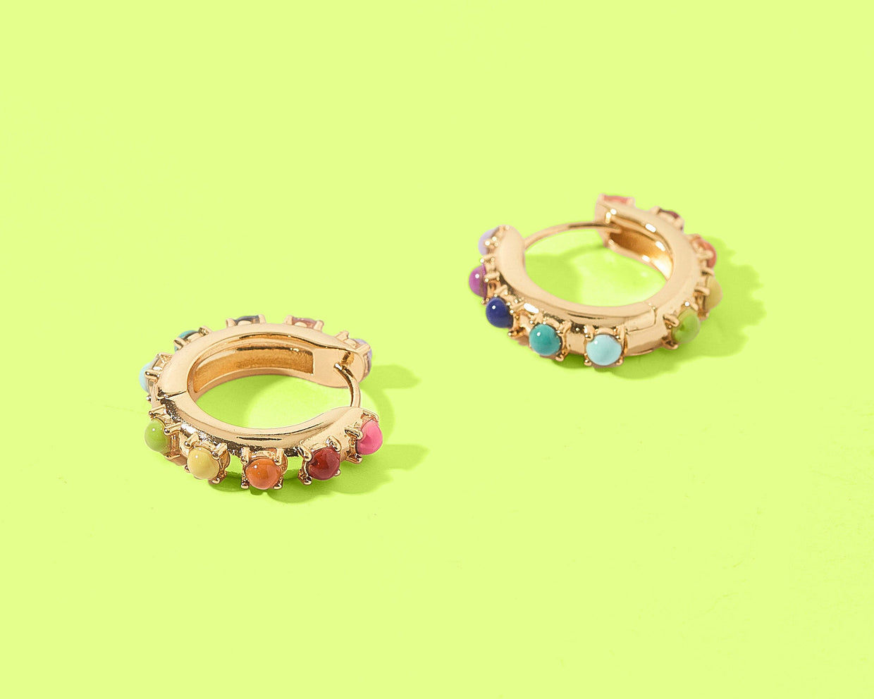 Pair of gold hoop earrings with colorful stones on a green background