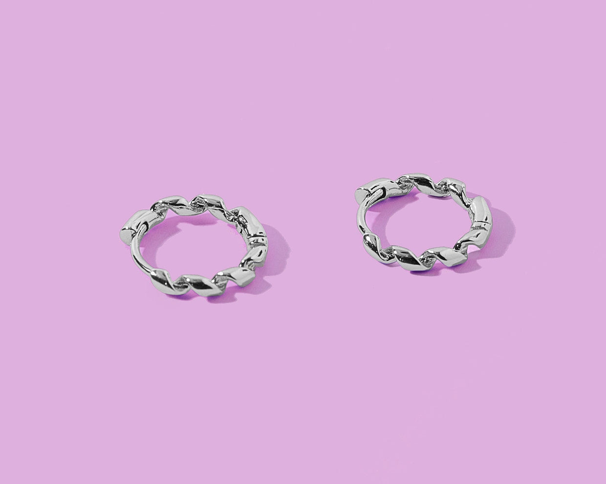 Pair of silver hoop earrings on a pink background